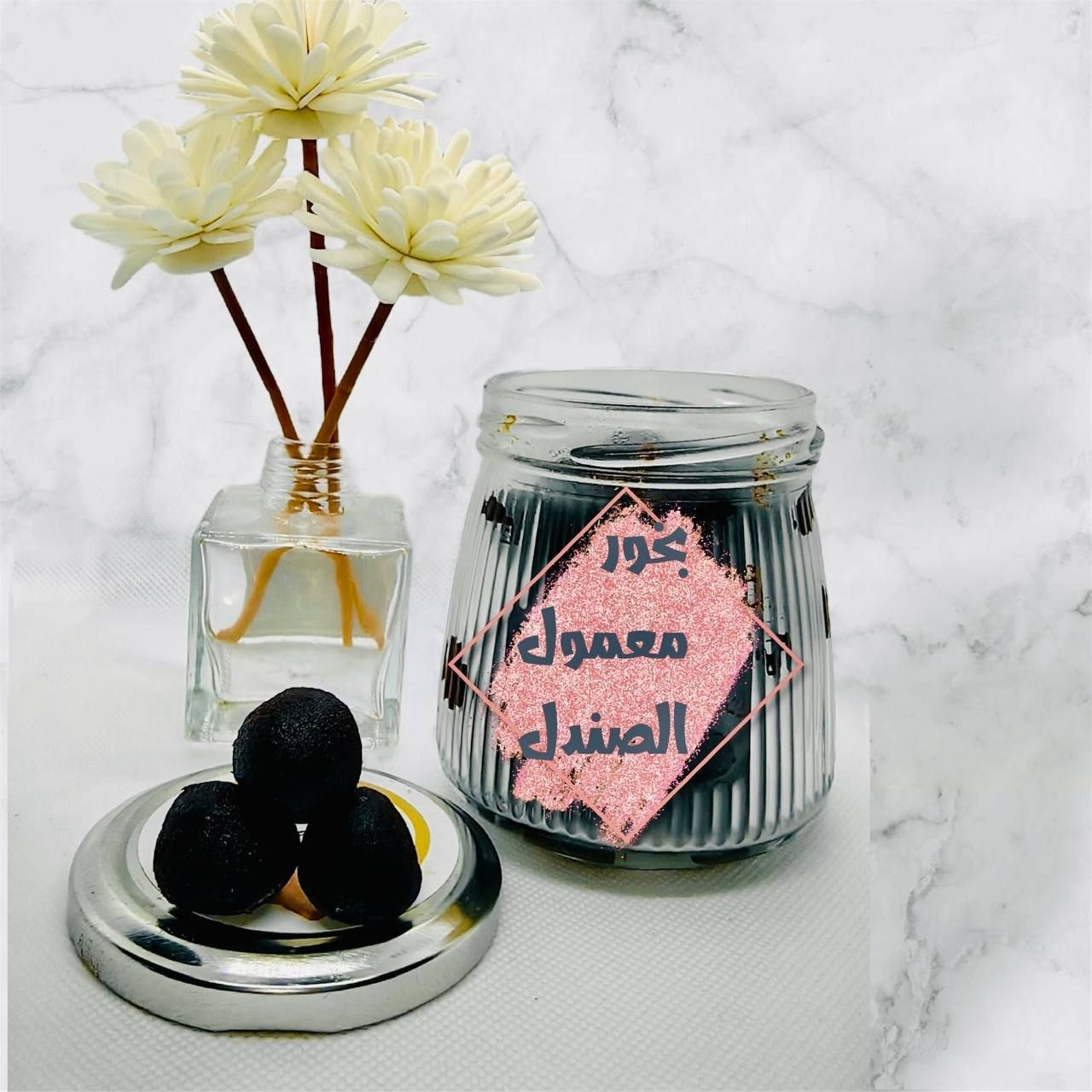 Glass jar with dark contents, lid, and decorative flowers in a vase on a marble surface.