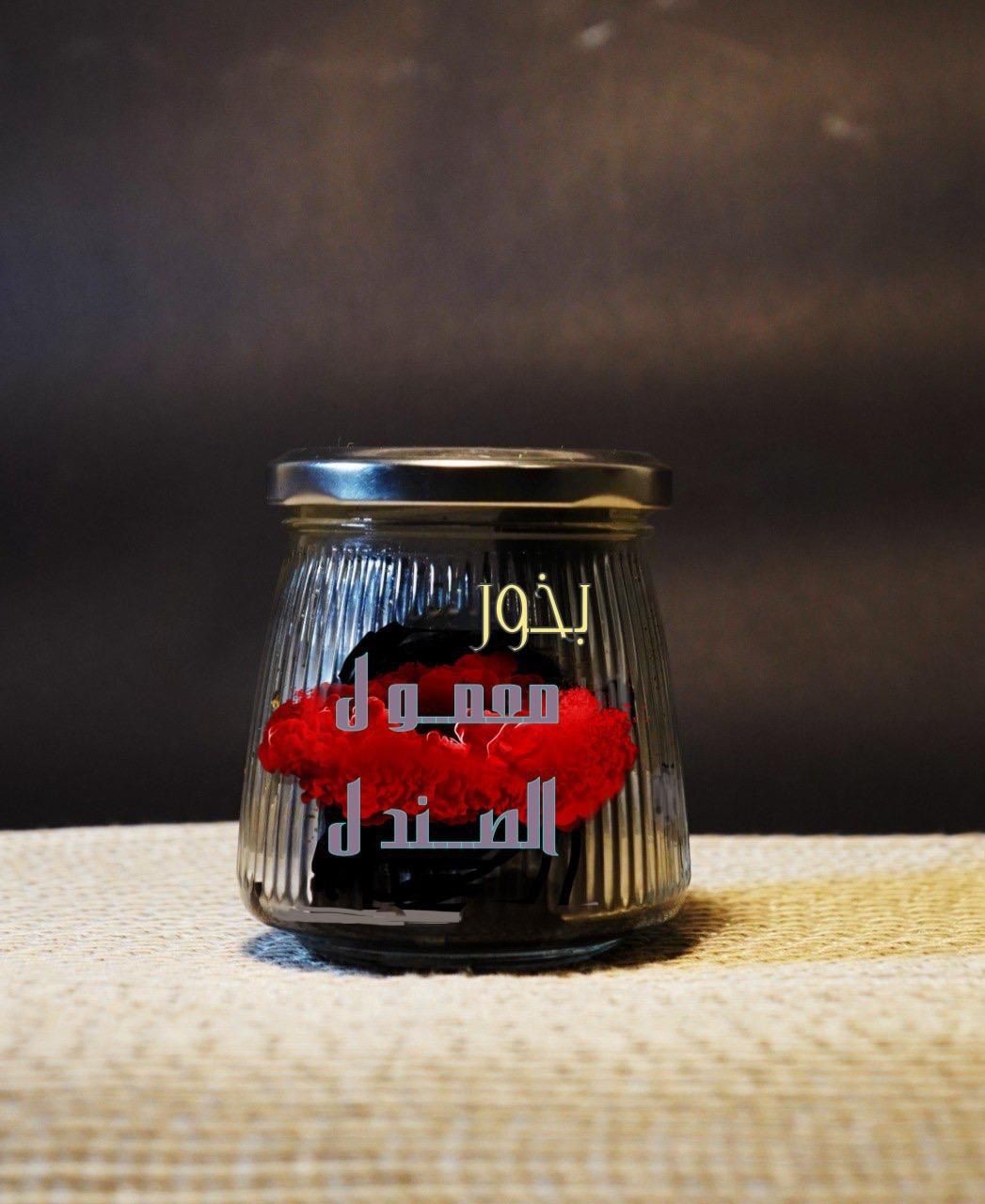 Glass jar with Arabic text containing red and black decorative items on a woven surface.