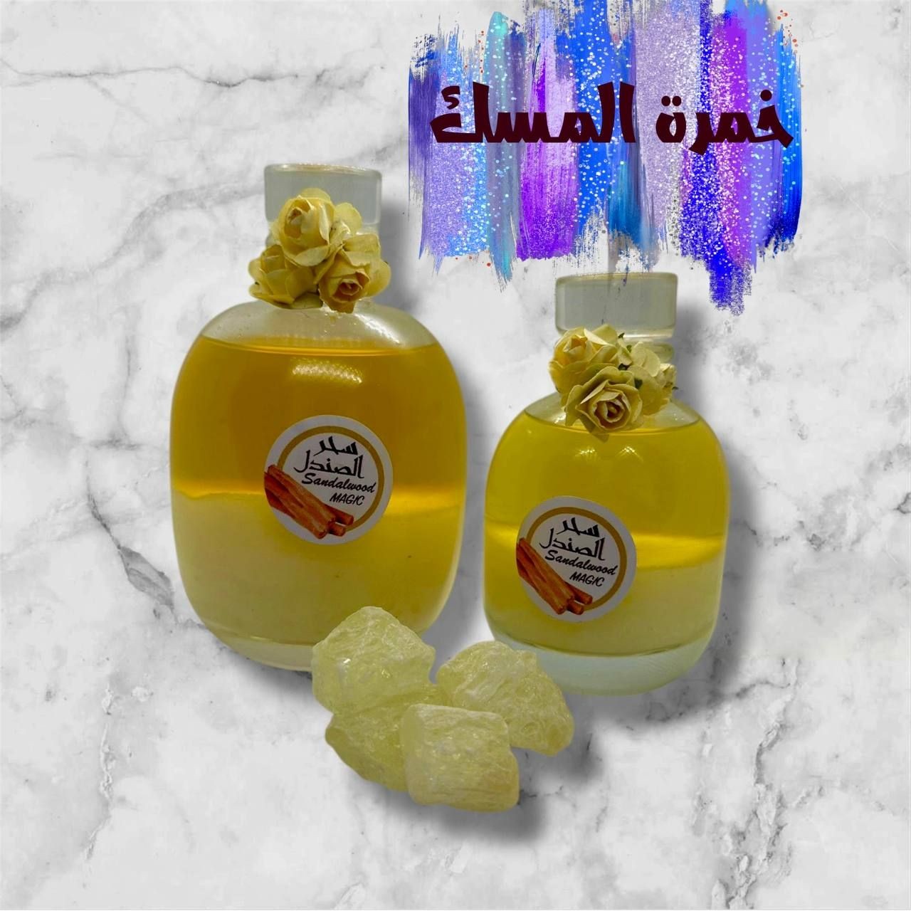 Two bottles of sandalwood musk with decorative flowers on a marble background and resin pieces in front.