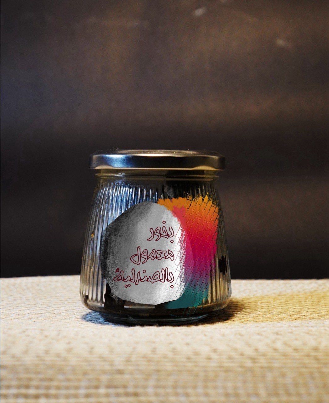 Glass jar with colorful geometric design and Arabic text on a textured surface.