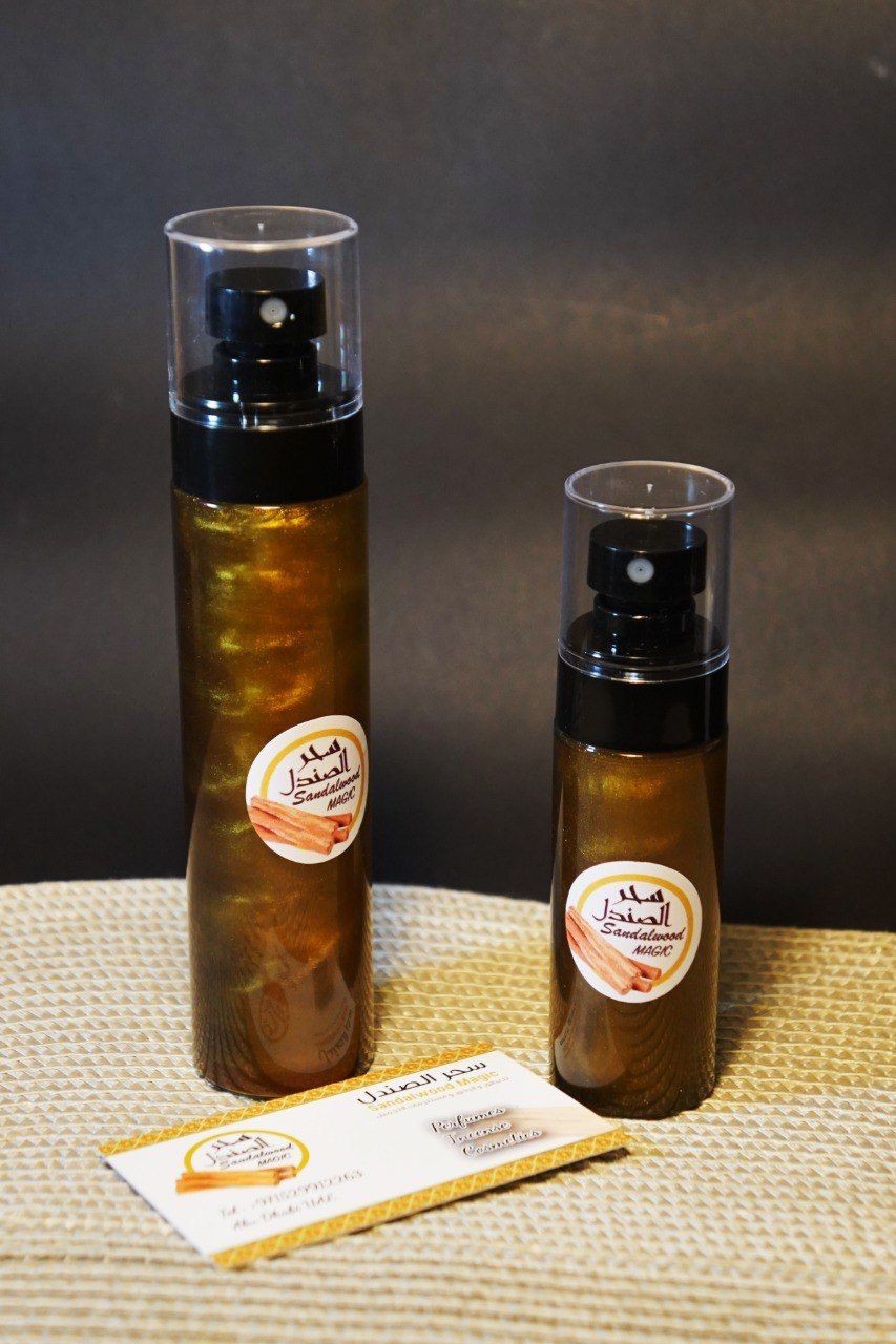 Two bottles of Sandalwood Magic perfume with a business card placed on a textured surface.